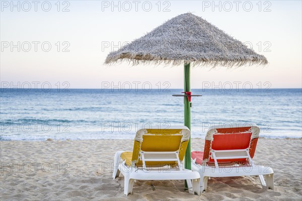 Colorful red and yellow sun beds under straw umbrellas on Falesia Beach