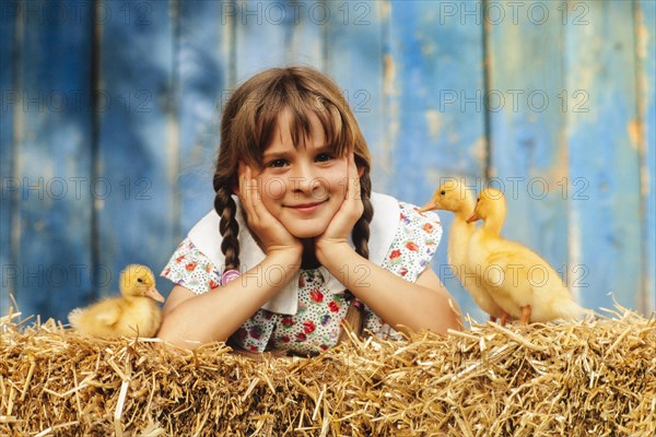 Nine year old girl lying with three ducklings in the straw