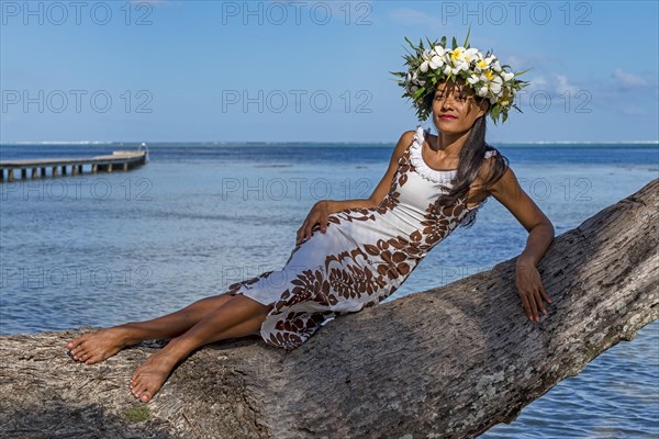 Young woman with flower wreath from Frangipani leaning on palm trunk