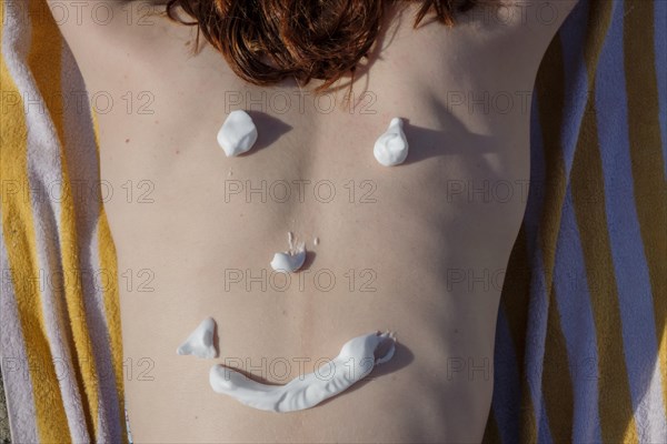 Red-haired young woman with sun cream on her back