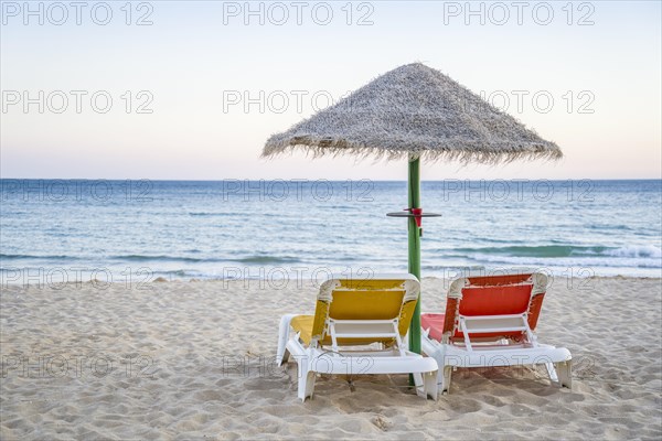 Colorful red and yellow sun beds under straw umbrellas on Falesia Beach