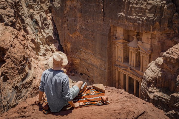 Tourist with sun hat sits on carpet and looks from above into the gorge Siq