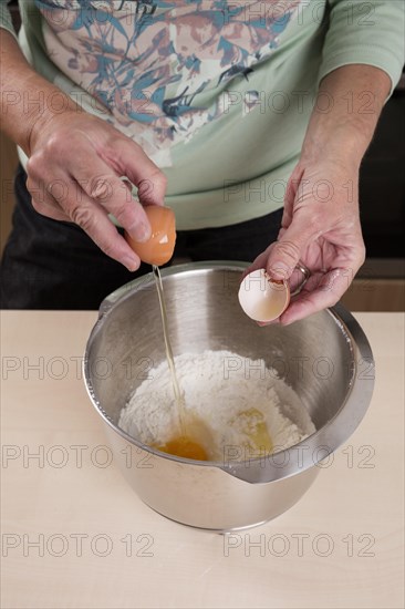 Woman putting egg in bowl of dough
