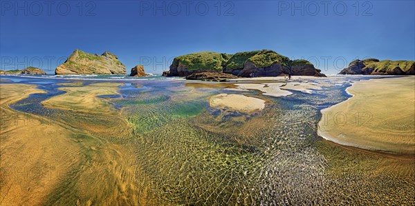 Sandy beach with receding water and rocky island in the surf