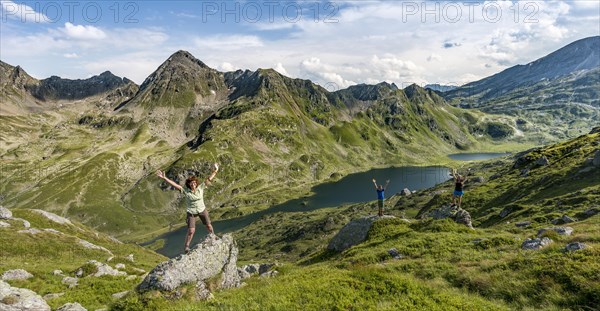 Three hikers standing on rocks in front of mountain landscape