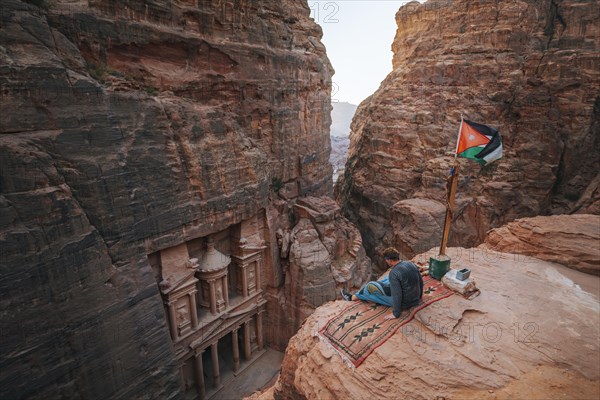 Tourist sits at the edge of a rock and looks from above into the canyon Siq