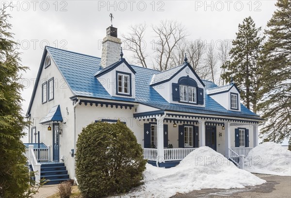 Old 1920s white roughcast with blue trim cottage style home facade with blue steel tile roof in early spring
