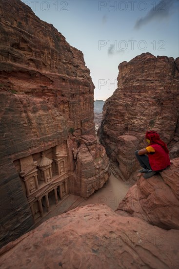 Bedouin sits at the edge of a rock and looks from above into the gorge Siq