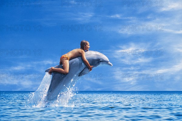 Six year old girl riding a dolphin leaping out of the sea