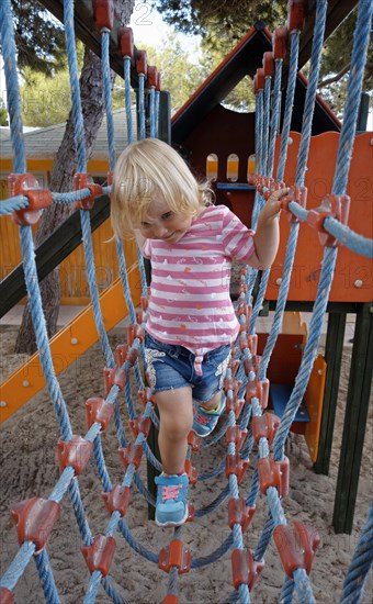 Two year old girl climbing rope bridge