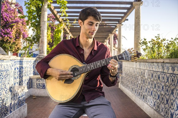 Fado musician playing on portuguese guitar under pergola in Alfama