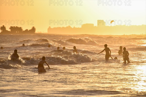 Many people bathing on the beach at sunset