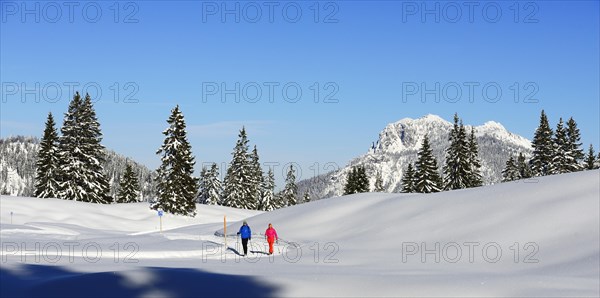 Two hikers walk through snow-covered mountain scenery