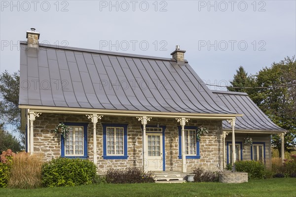 Old 1820 cottage style fieldstone house facade with blue trim and brown standing seam sheet metal roof plus stacked log extension in autumn