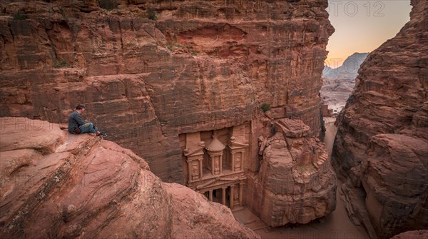 Tourist sits at the edge of a rock and looks from above into the canyon Siq