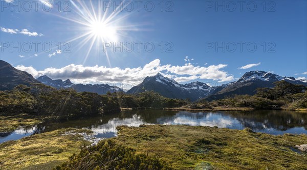 Sun shining on small mountain lake with reflection of a mountain chain