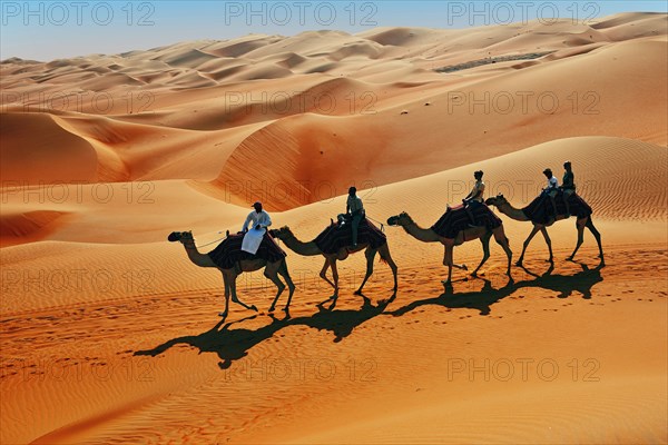 Tourists on camel ride in front of high sand dunes