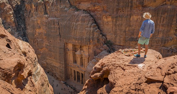 Tourist with sun hat stands on rocks and looks from above into the gorge Siq