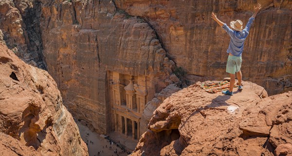 Tourist with sun hat stands on rocks with raised arms and looks from above into the gorge Siq