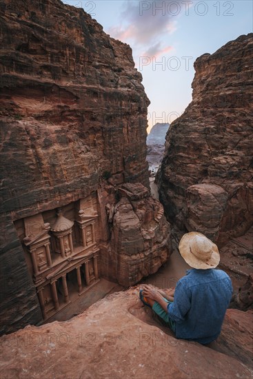 Tourist sits at the edge of a rock and looks from above into the canyon Siq