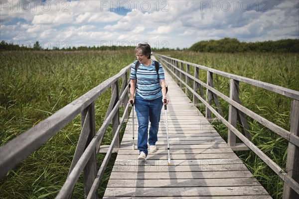 Elder woman walks on crutches on Federsee walkway