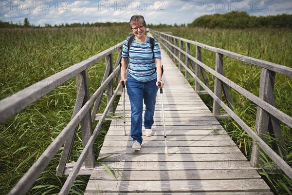 Elder woman walks on crutches on Federsee walkway