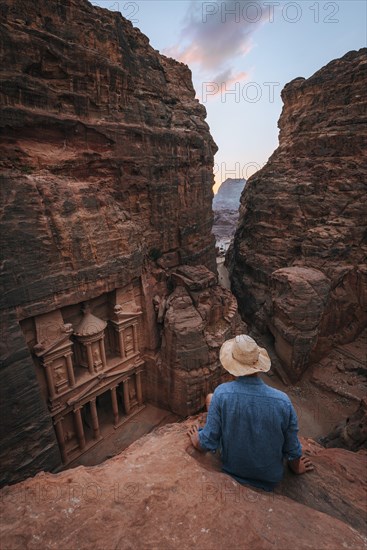 Tourist sits at the edge of a rock and looks from above into the canyon Siq