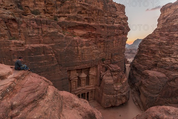 Tourist sits at the edge of a rock and looks from above into the canyon Siq