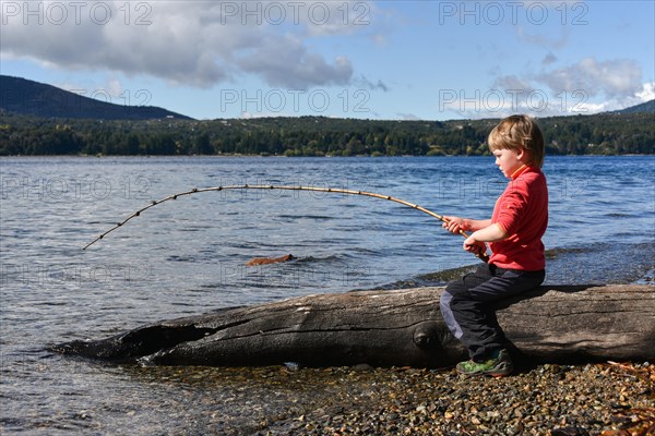 Small boy sitting on a tree trunk fishing at Lake Nahuel Huapi