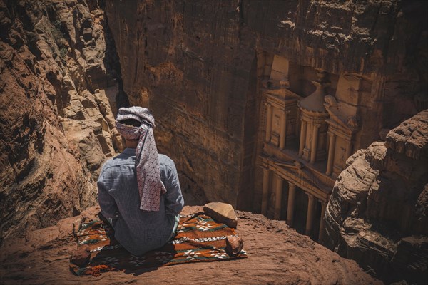 Tourist with turban sits on carpet and looks from above into the canyon Siq