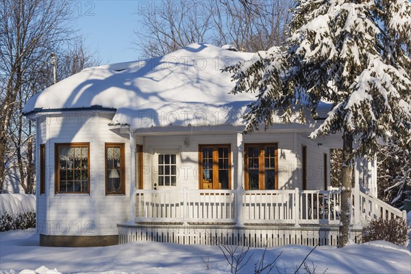 Old white wood plank cladded house facade with brown trim and blue sheet metal roof in winter