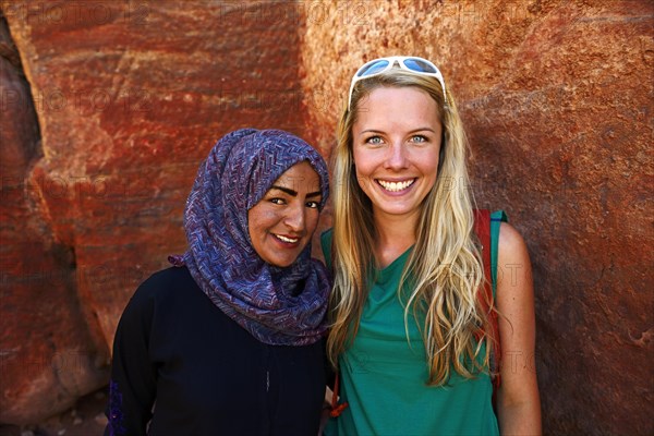 Tourist girl poses with local bedouin girl at colourful rock-formations in Petra