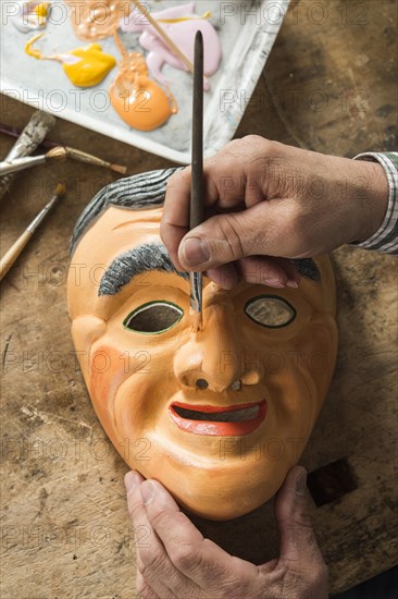 Painting the face of a wooden mask with a paintbrush