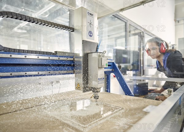 Woman with ear protection operates CNC milling machine