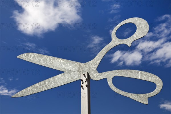 Oversized scissors in front of cloudy sky