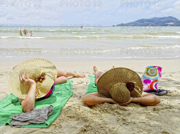 Women with large sun hats sunbathing on the beach