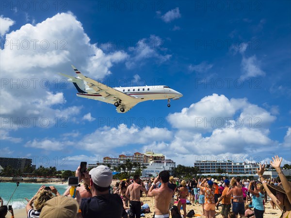 Tourists watching and photographing an airplane landing over Maho Beach