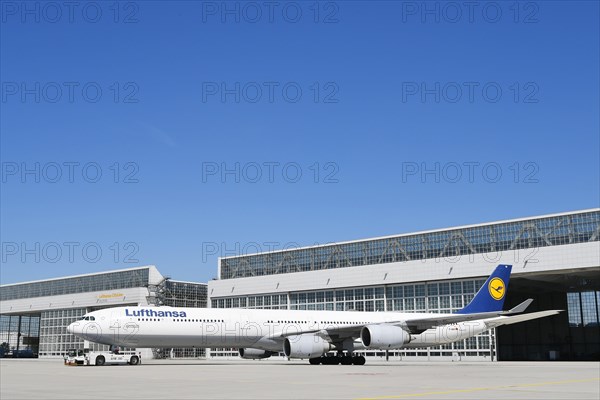 Lufthansa Airbus A340 with push-back truck in front of maintenance hangar