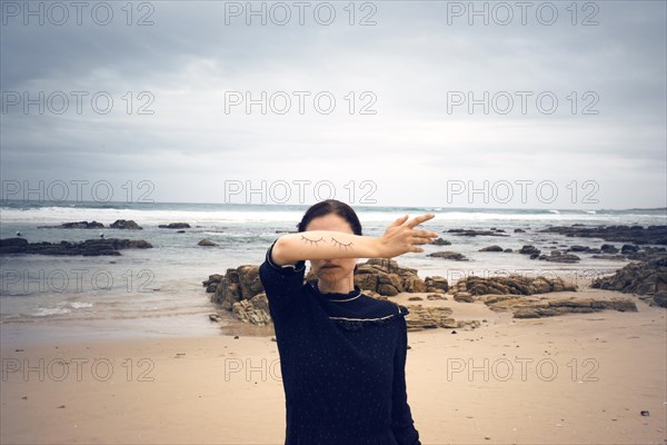 Woman with closed painted on eyes on her arm standing on the beach