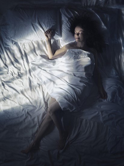 Young woman sleeping alone in bed at night in dark bedroom