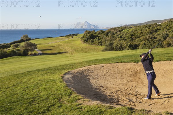 Golfer hitting from bunker at La Alcaidesa Golf Resort with Mediterranean Sea and Rock of Gibraltar
