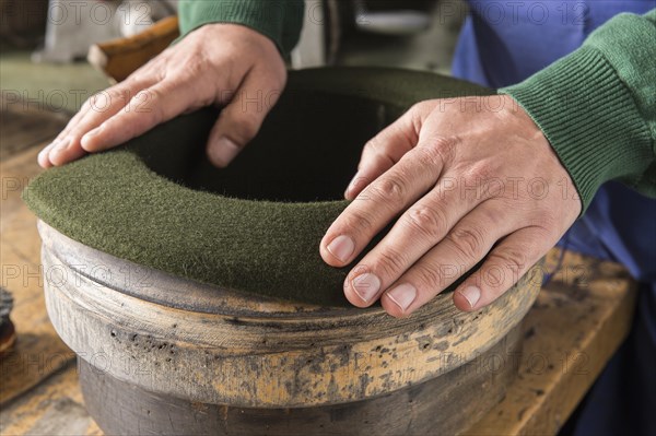 Hands shaping dry wool felt hat over edge mold