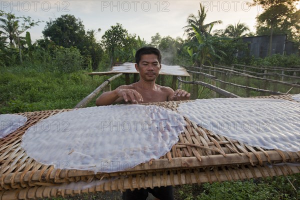 Vietnamese worker spreads steaming rice noodle patties on bamboo frame to dry