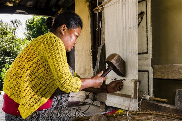 Native woman knotting carpet using sheep's wool in front of house