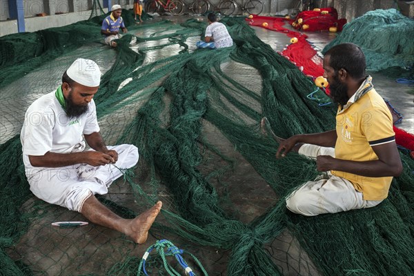 Local men repairing fishing nets in hall at harbour