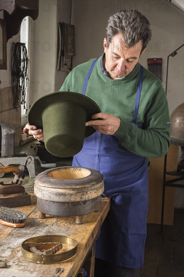 Hatter holding dry wool felt hat over an edge mold