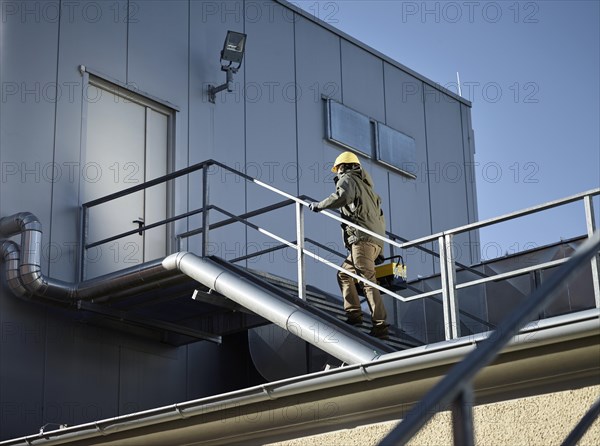 Engineer with yellow helmet and tool box using a staircase to an engine room
