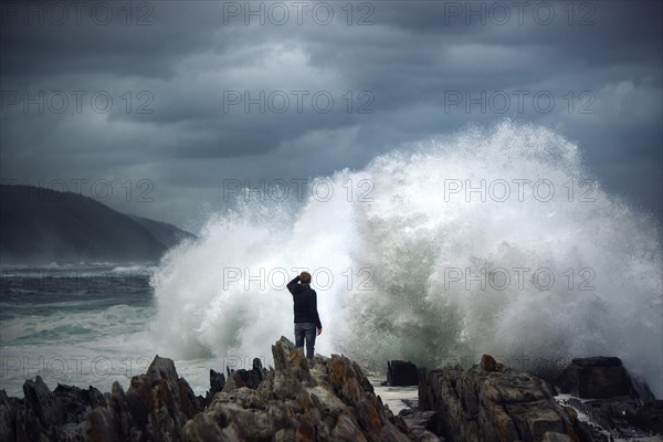 Man on rock in front of breaking wave