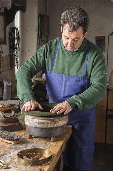 Hatter pushing dry wool felt hat into edge mold