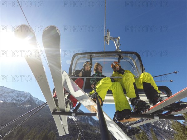 Three teenagers on chairlift with skis and snowboard